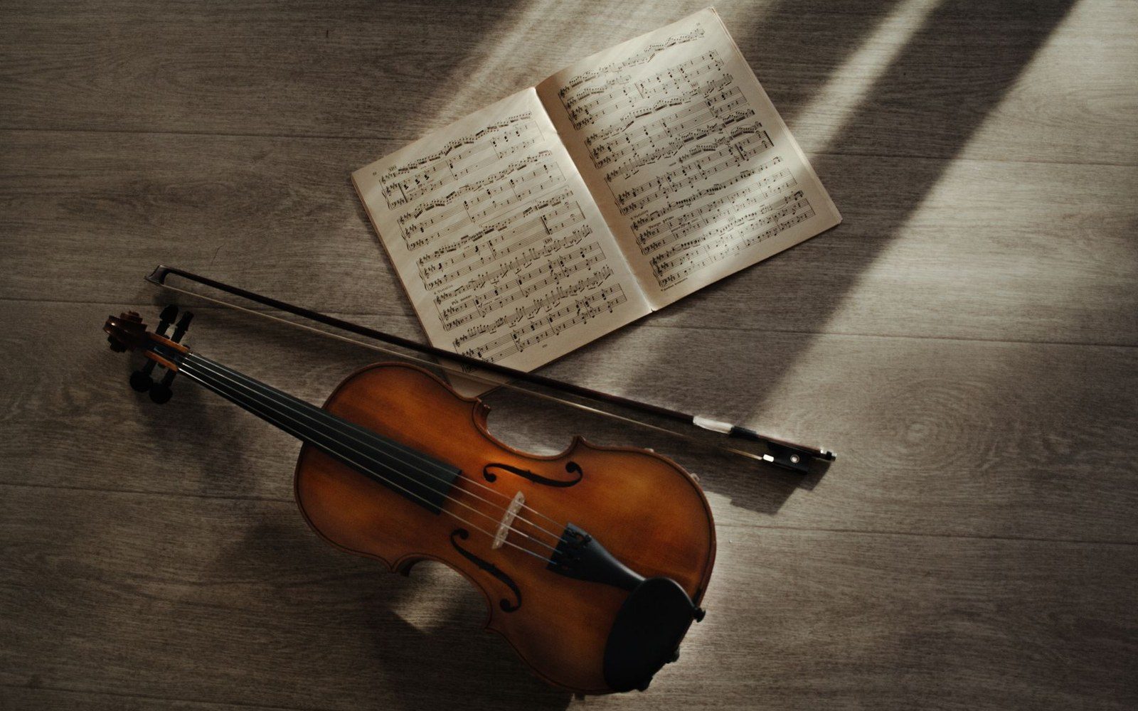 Violin and bow resting beside an open sheet music book on a wooden floor